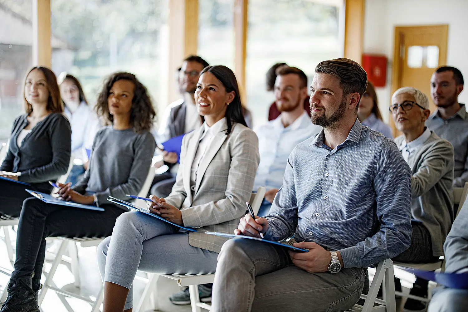 Several people in a bright room are listening to a lecture.